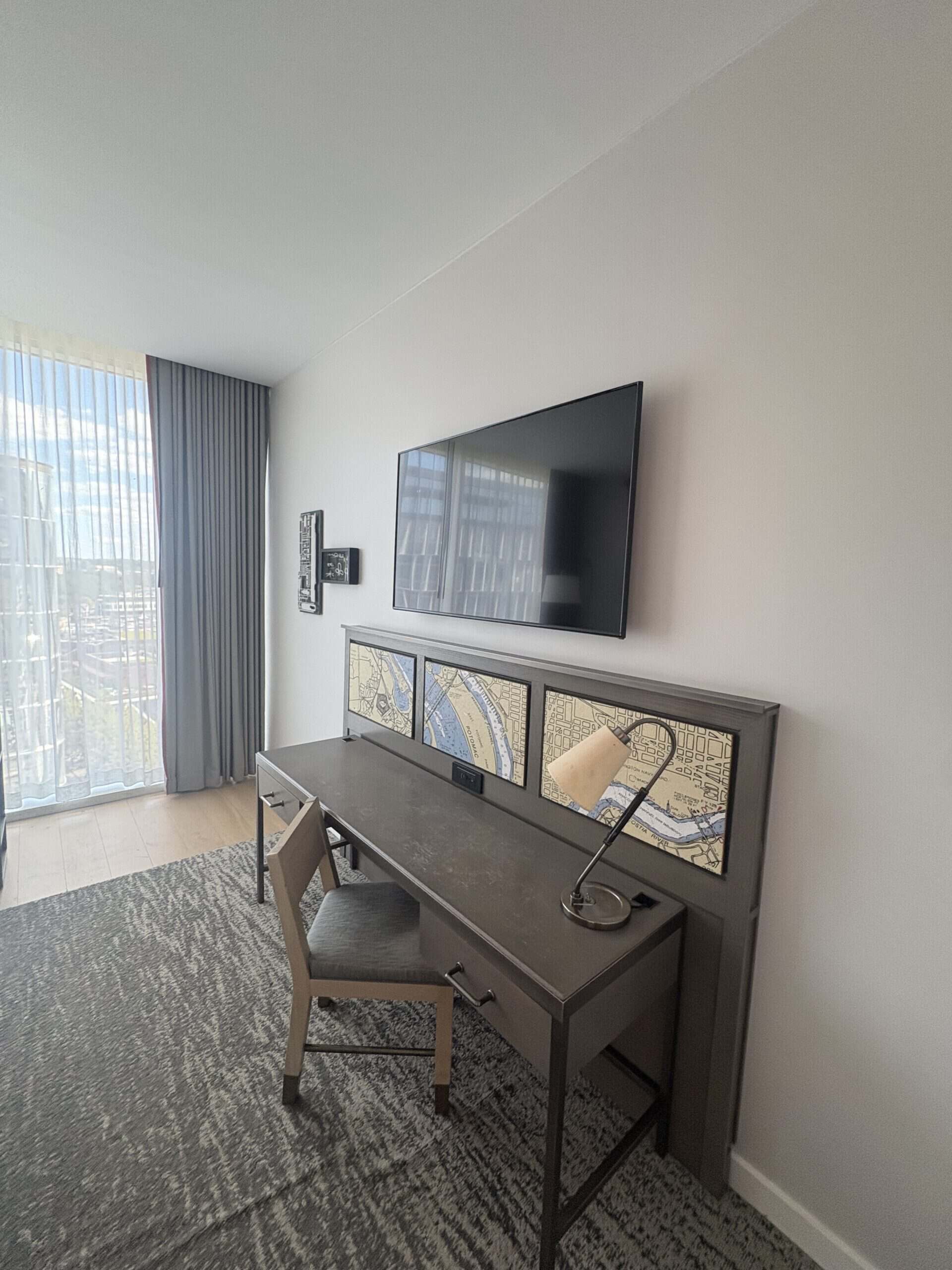 Desk with nautical map artwork panels and wall-mounted TV at Canopy by Hilton Washington DC The Wharf